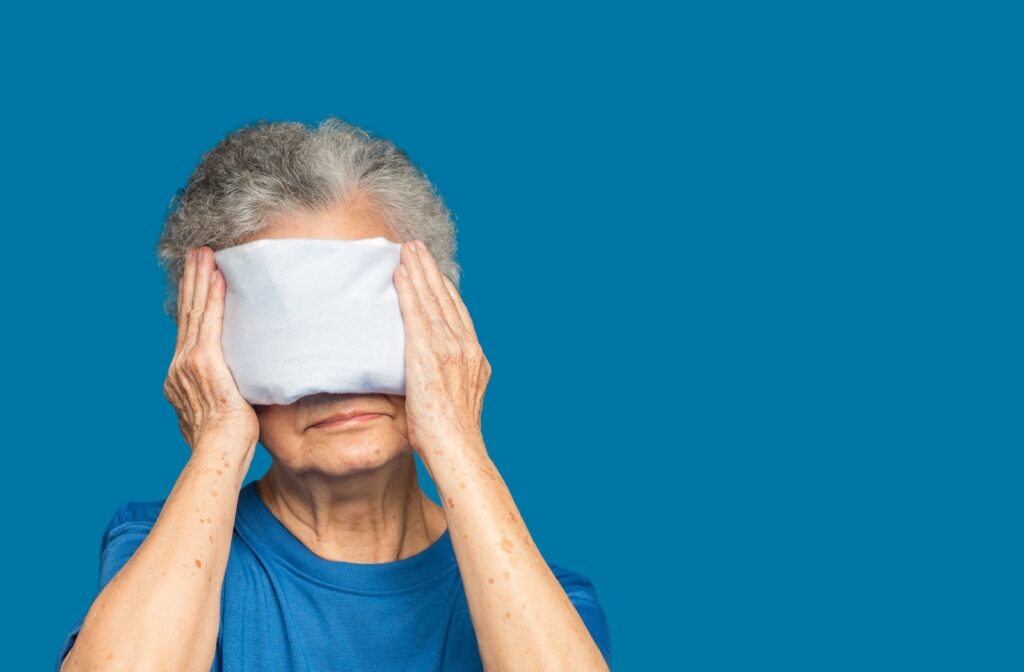 A mature woman holds a hot compress against her eyes.