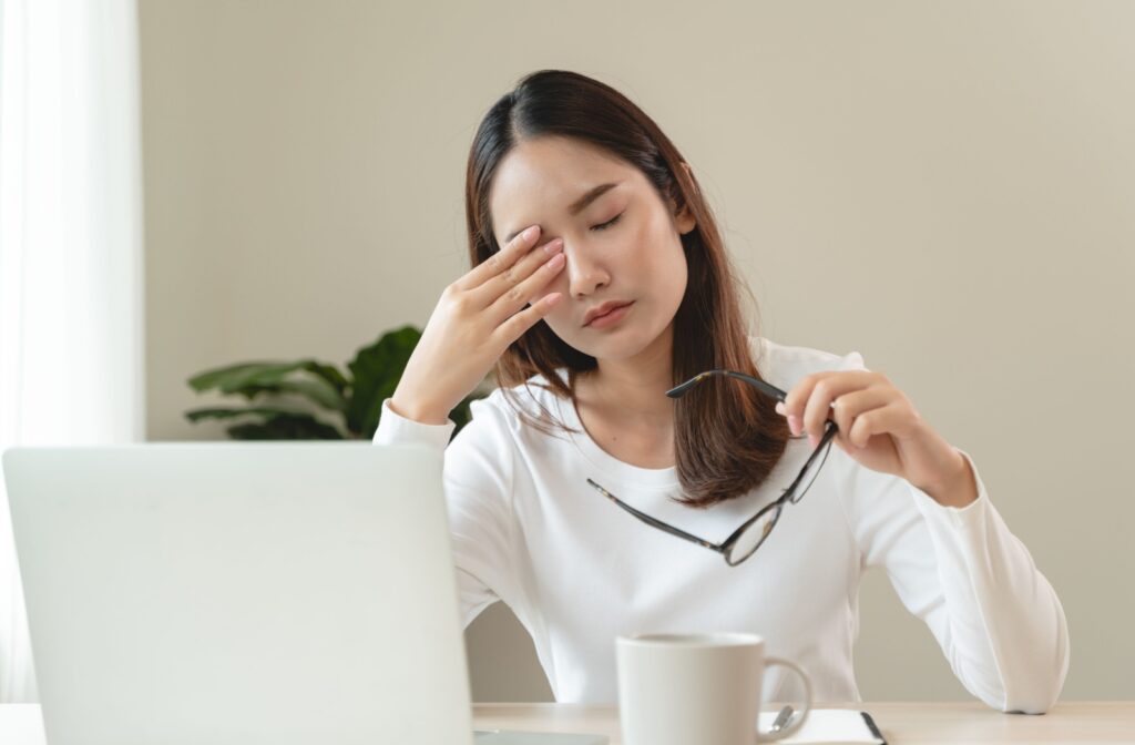 A woman rubs her dry eyes while sitting in front of the computer.