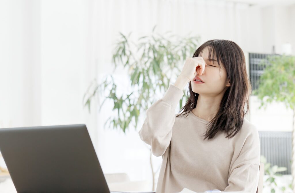 Young woman experiencing eye discomfort while working on a laptop, highlighting the potential benefits of IPL and RF treatments for dry eye relief.