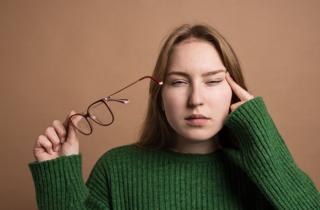 A person holding glasses in one hand and squinting from foggy vision.